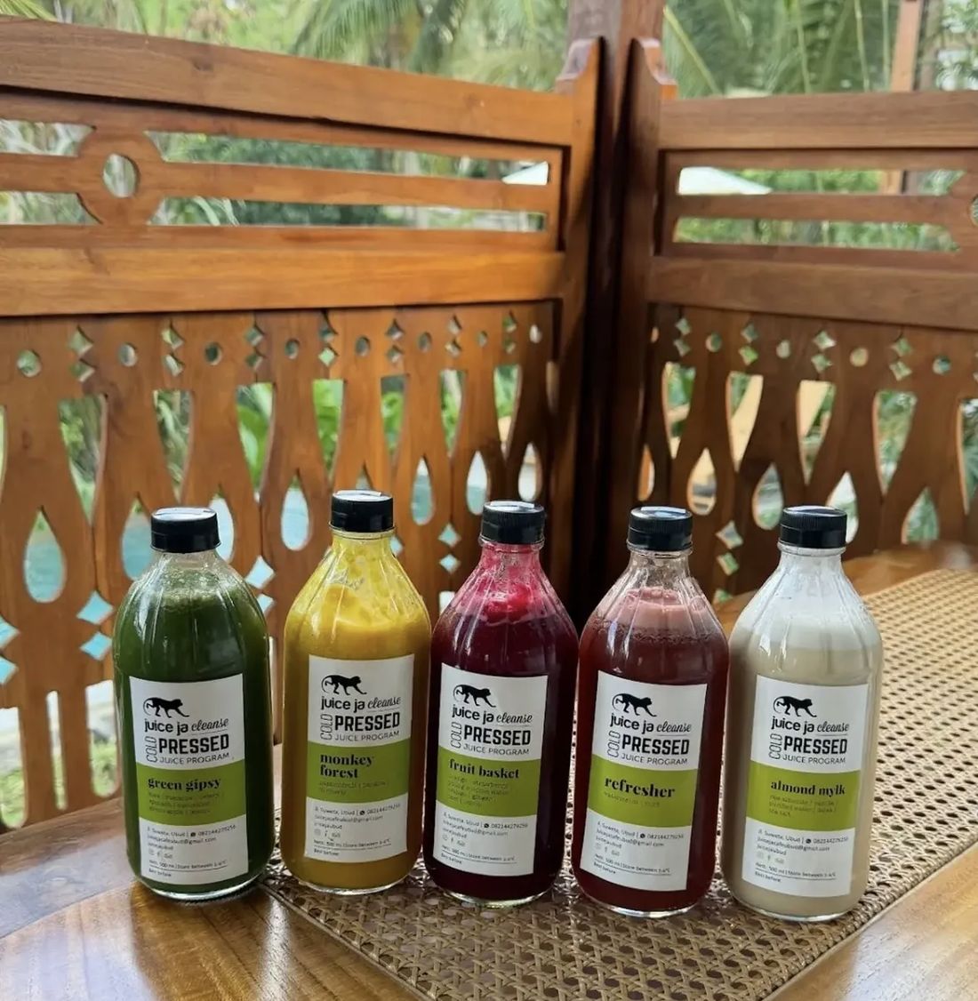 Five cold-pressed juice bottles from the Juice Ja cleanse lined up on a wooden table