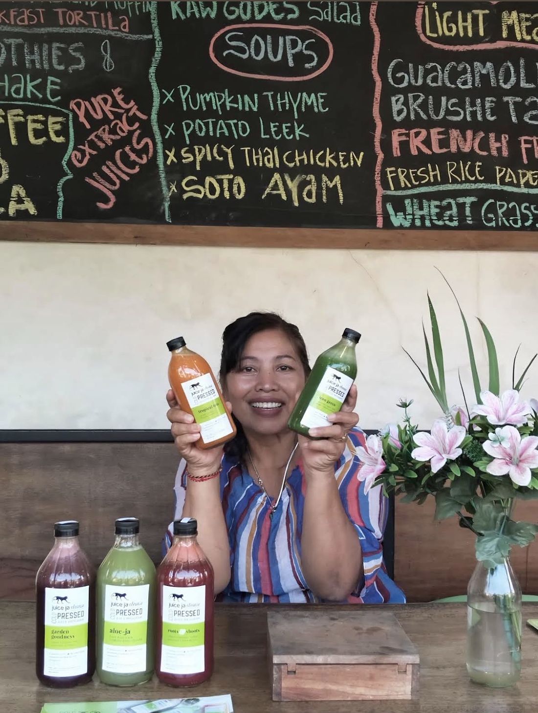 Ibu Rika, owner of Juice Ja Café, smiling and holding two bottles of cold-pressed juice